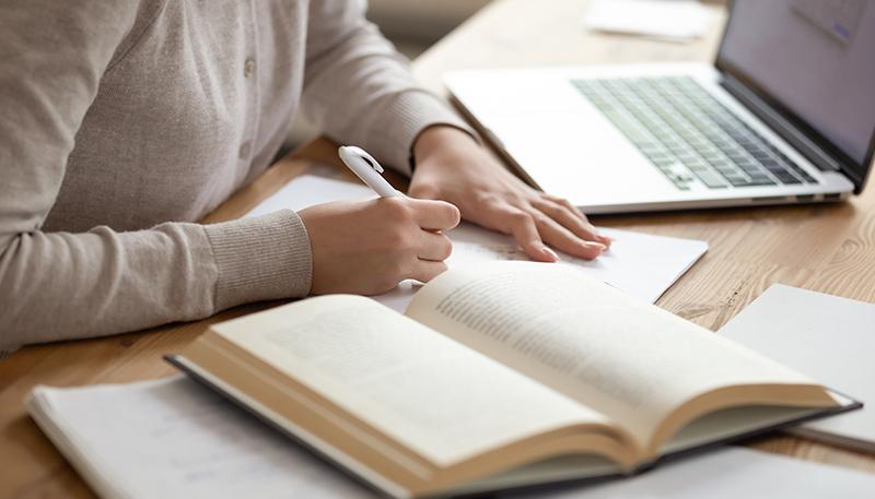 Close up female student writing down notes from opened textbook.