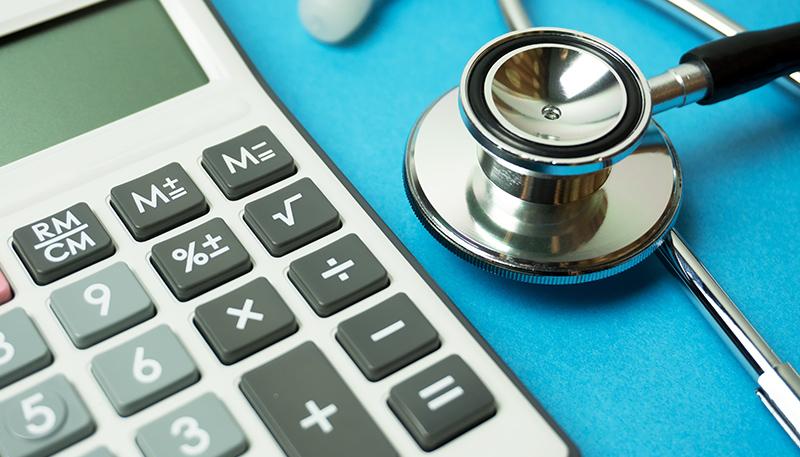 Close up of calculator and stethoscope on blue background - Business and Insurance concept