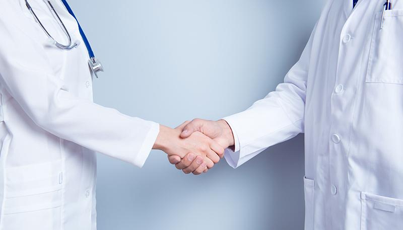 Deal! Concept of collaboration in medicine. Close up photo of two doctors' handshake on gray background