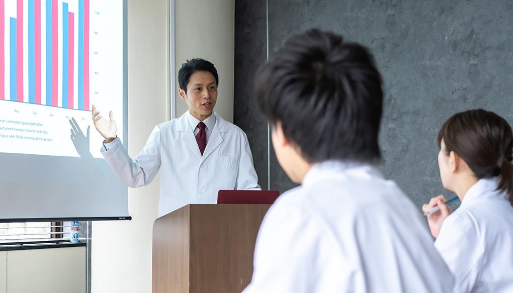 若い医師の前で講義をする医療安全管理者の男性医師