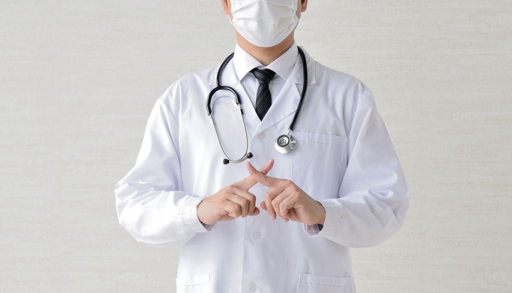 指でバツを作る医師の写真